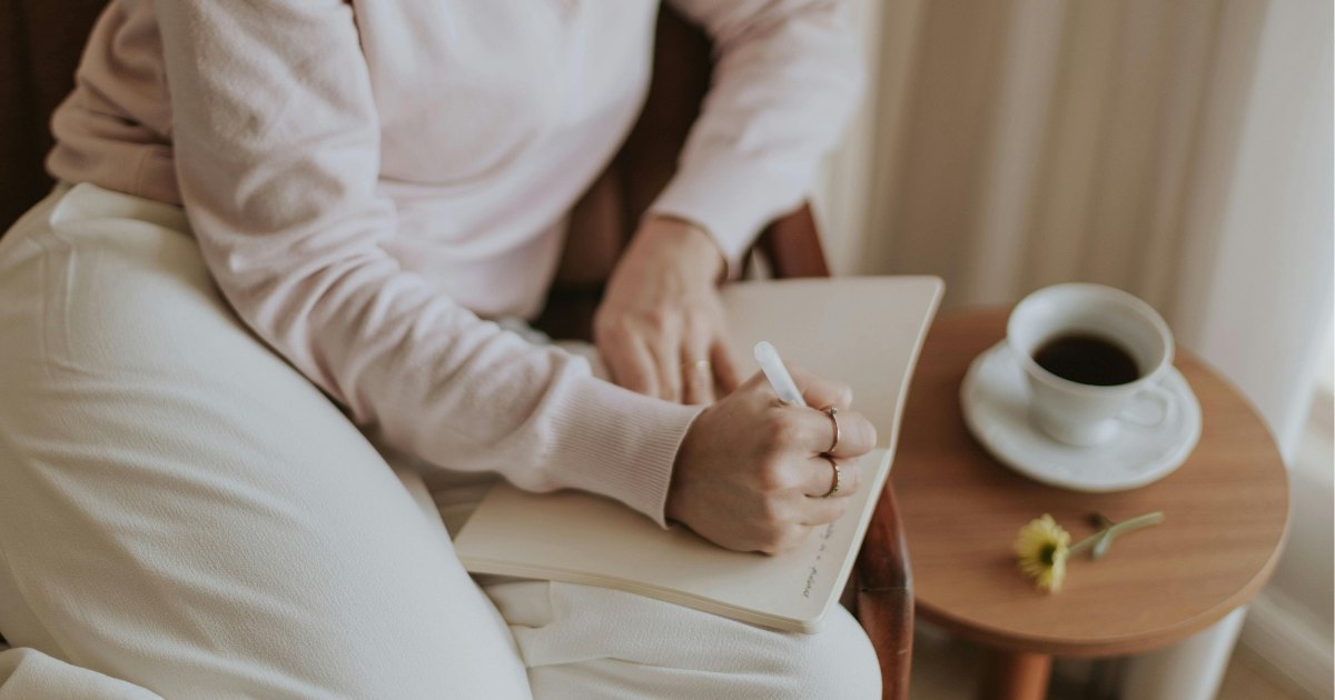 Mum writing in a notebook beside a cup of coffee